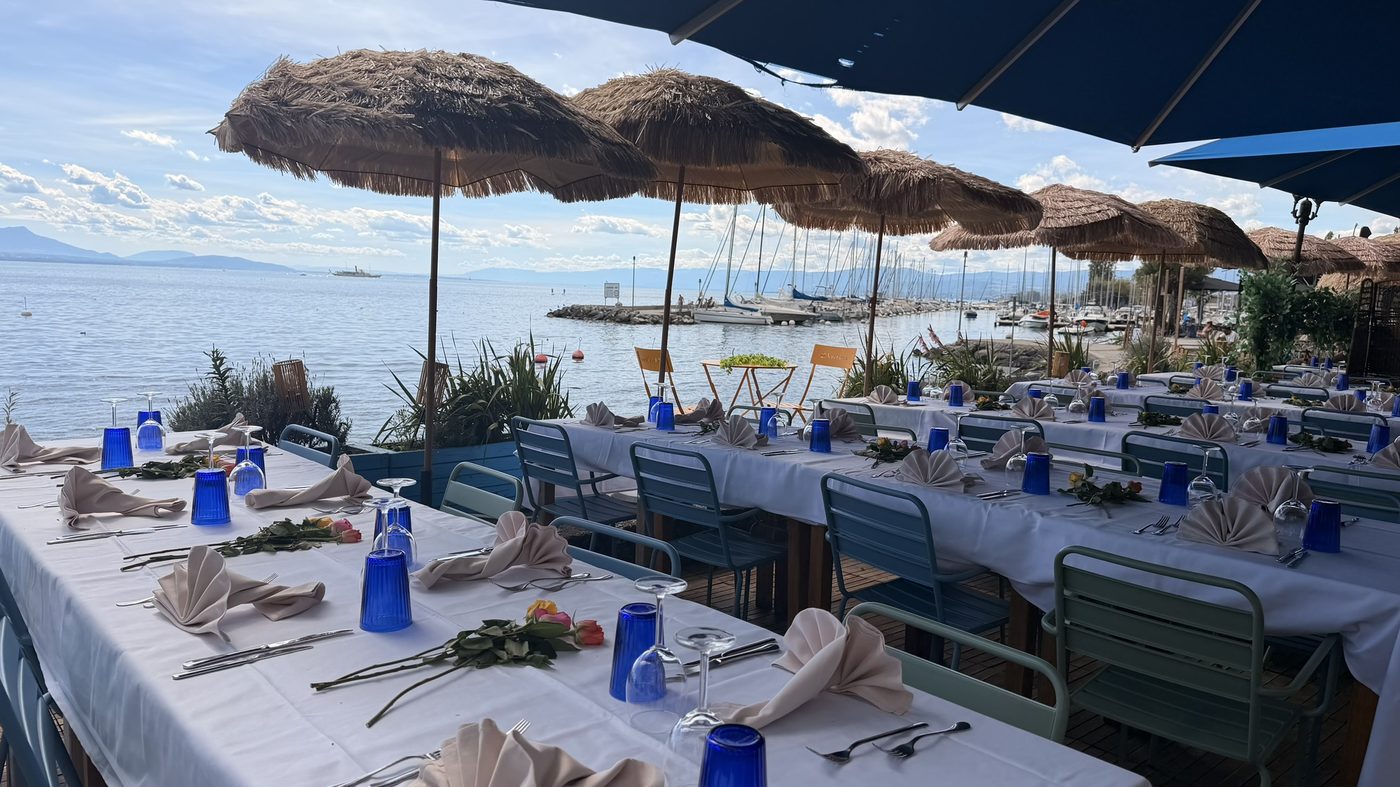 Tables dressées sous les parasols de paille, roses et verres bleus face au lac
